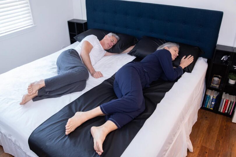 Two adults sleep on a bed with a black grounding sheet running along one side under their bodies